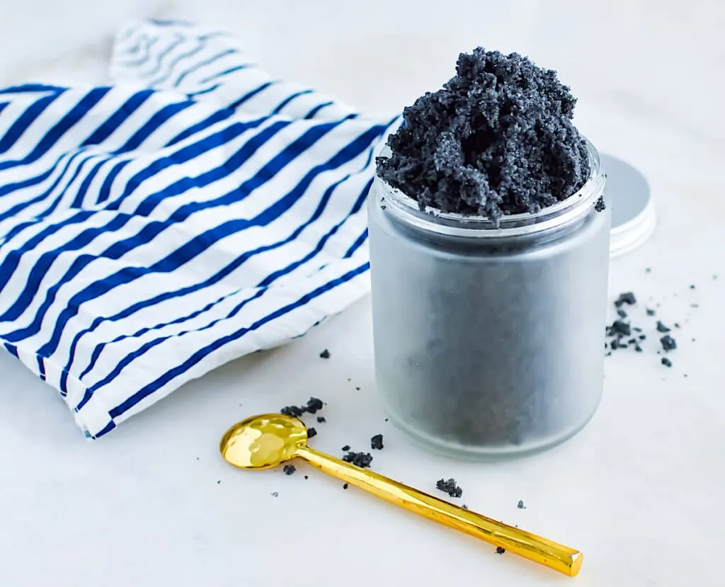 Activated Charcoal Scrub in a jar on a white table with a blue and white striped linen cloth