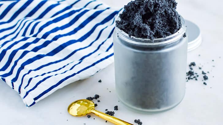 Activated Charcoal Scrub in a jar on a white table with a blue and white striped linen cloth