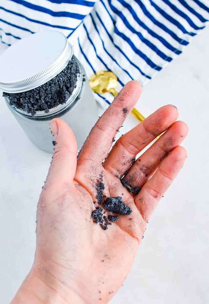 Activated Charcoal Scrub clumped in personas hand with jar of scrub in background