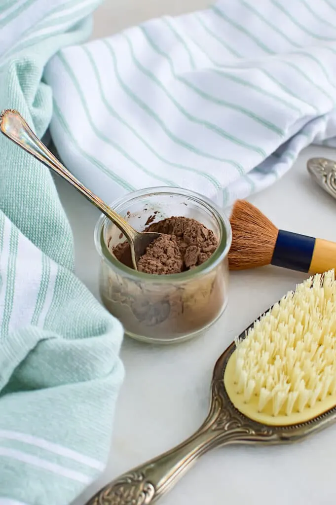 A jar of cocoa powder and a brush are placed on a table.