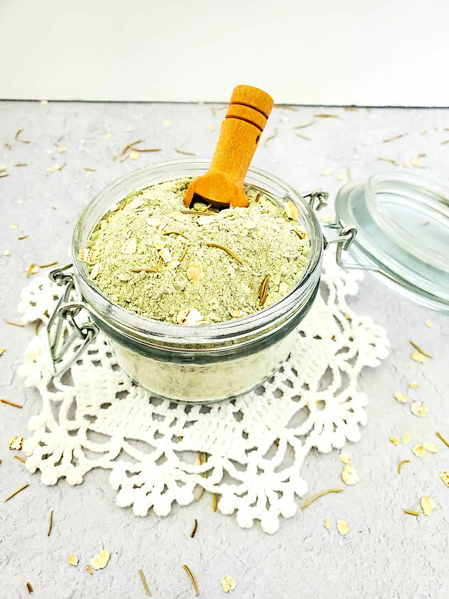 A clear glass jar with a wood spoon containing a Detox Clay Bath mixture.