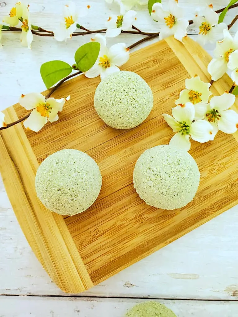 Three green lemongrass bath bombs on a wooden cutting board.