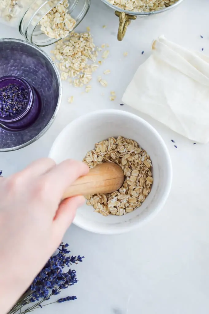 A person is mixing oats with a wooden spoon while making Oat Bath Soak.