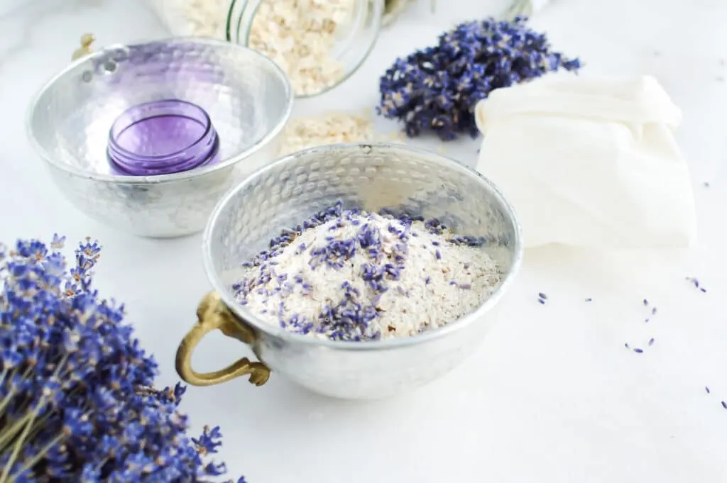 A bowl of oats and lavender flowers on a table making Oat Bath Soak.