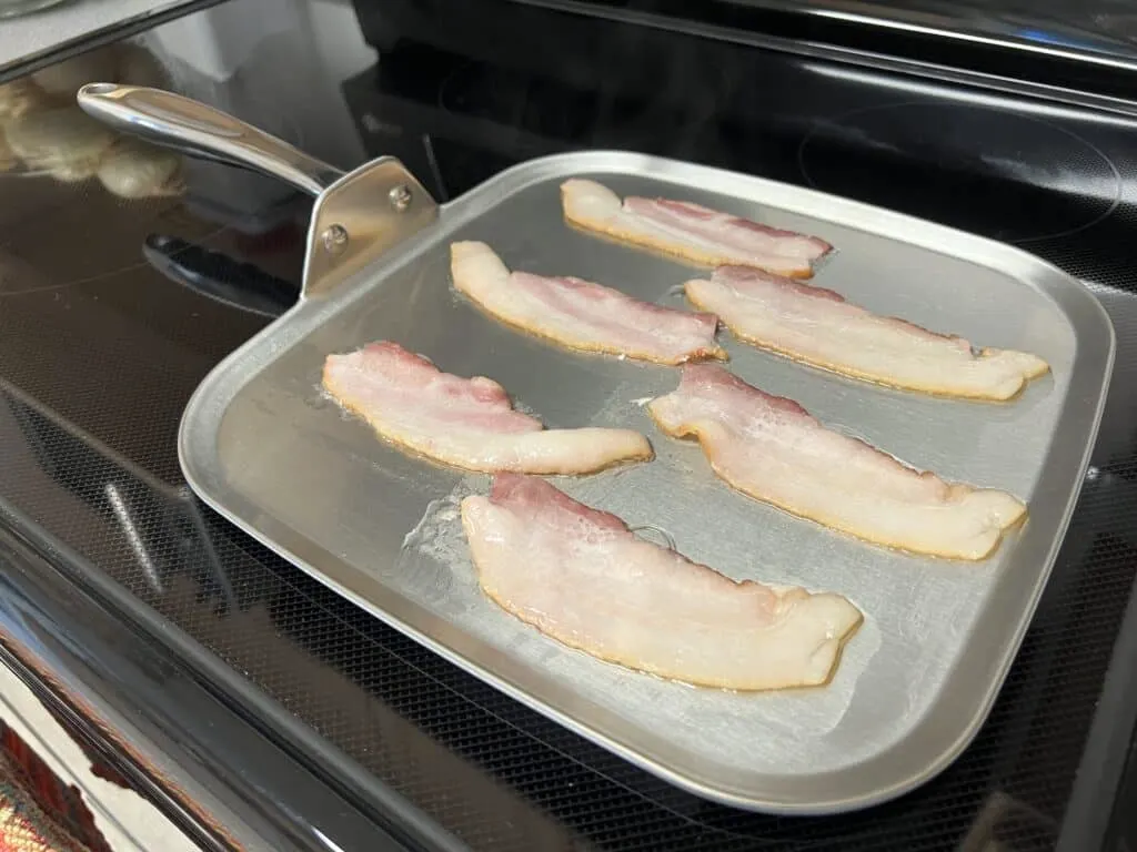 https://www.getgreenbewell.com/wp-content/uploads/2023/12/frying-bacon-in-360-cookware-griddle-pan-1024x768.jpeg.webp
