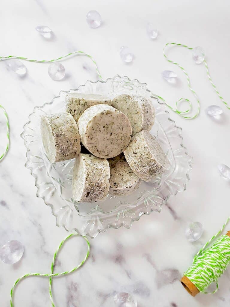 Peppermint Shower Steamers in a clear glass bowl with green twine on a white marble surface.