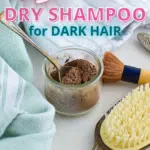 Image showing a DIY dry shampoo for dark hair setup. It includes a jar with powder, a spoon, a brush, a striped towel, and a hairbrush placed on a white surface.